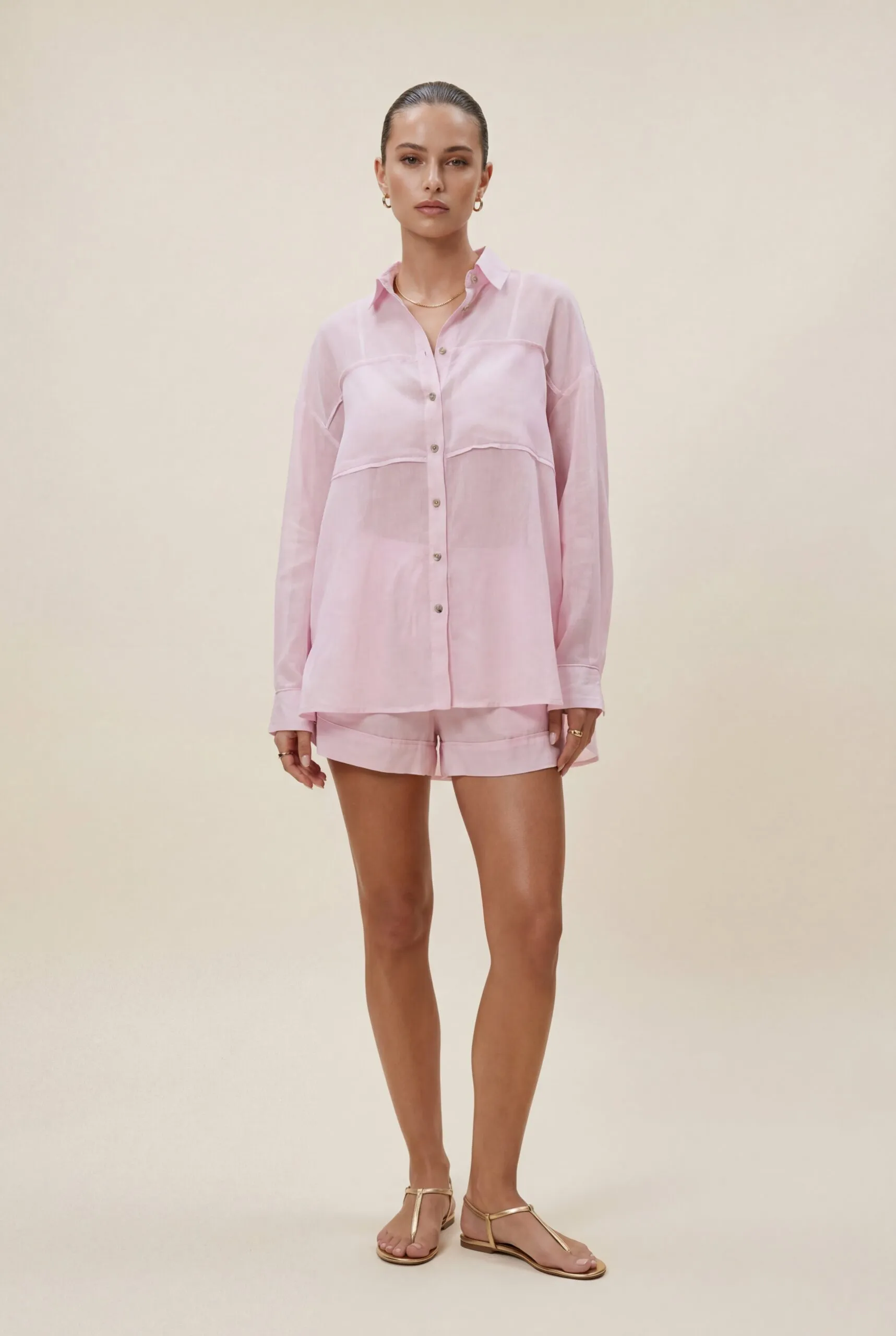 ‘s wearing minimal gold jewelry and gold flat sandals . shirt should be put in the shorts only in one side